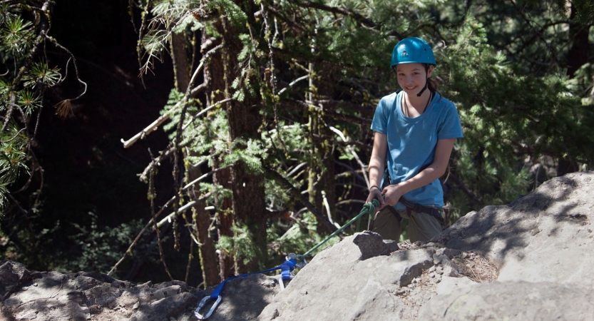 an outward bound student wearing rock climbing gear smiles at the camera 